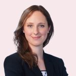 Porträt einer jungen Frau mit langen Haaren in dunklem Blazer vor hellem Hintergrund.