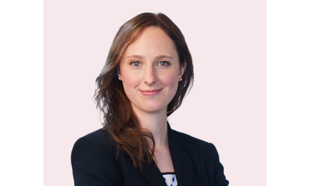 Porträt einer jungen Frau mit langen Haaren in dunklem Blazer vor hellem Hintergrund.