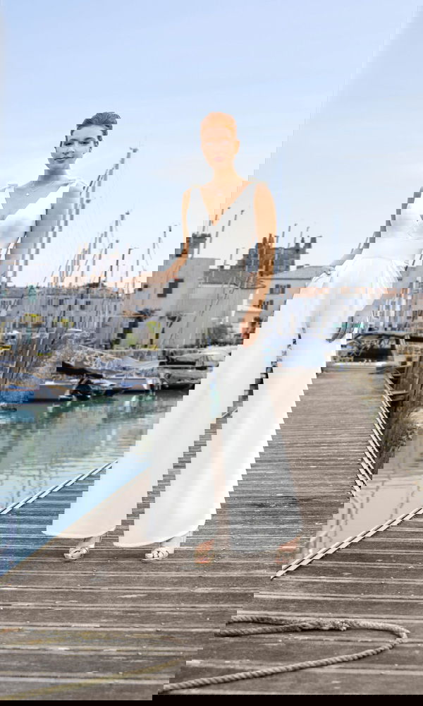 Minimalistische bruidsjumpsuit met diepe V-hals en wijde pijpen, gefotografeerd op een houten steiger in een havenomgeving.