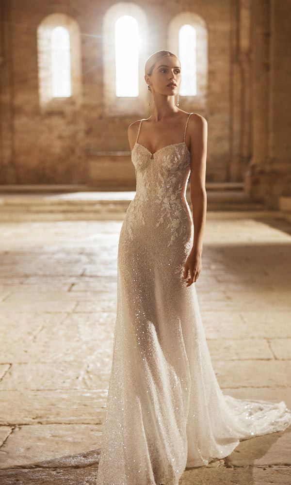 Sprankelende bruidsjurk met slanke snit, fijne bandjes en een volledig met pailletten en mini-parels bezette stof in een historisch interieur.