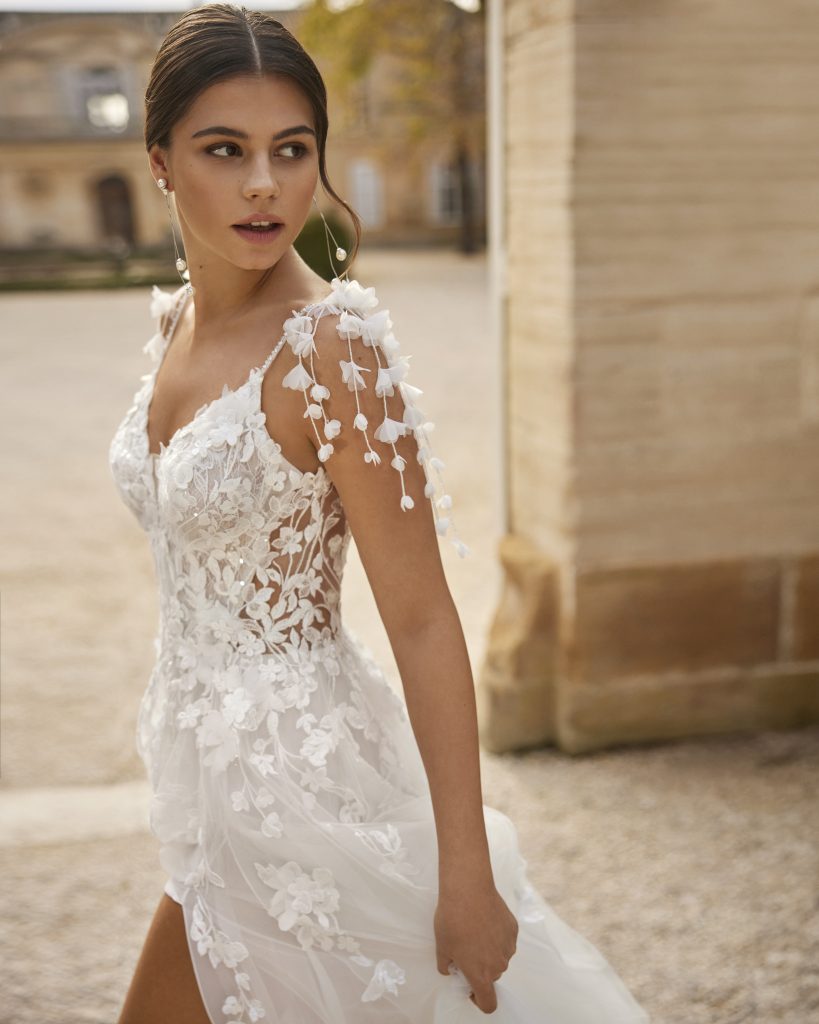 Romantische A-lijn bruidsjurk met fijne kant en 3D-bloemen op de schouders, gefotografeerd in een elegante, stedelijke setting.