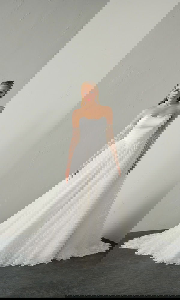 Strapless baljurk met strak lijfje en transparante kanten mouwen, gefotografeerd in een minimalistische studio-opstelling.