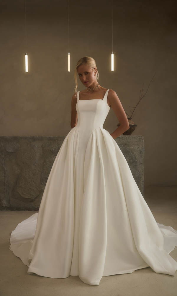 Minimalistische baljurk met Basque-taille, rechte halslijn en volumineuze rok in een serene, moderne setting.