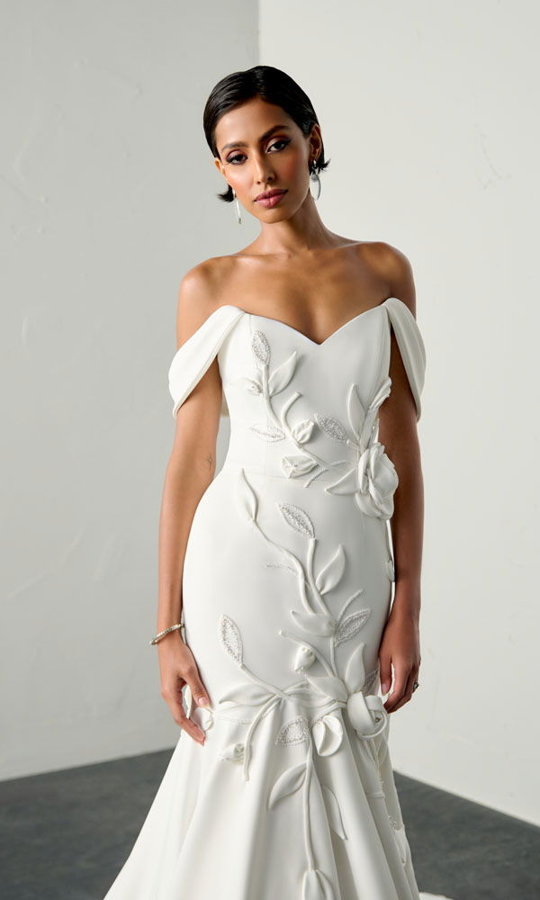 Fit-and-flare bruidsjurk met off-shoulder halslijn en grote florale applicaties, verrijkt met parels in verschillende formaten.