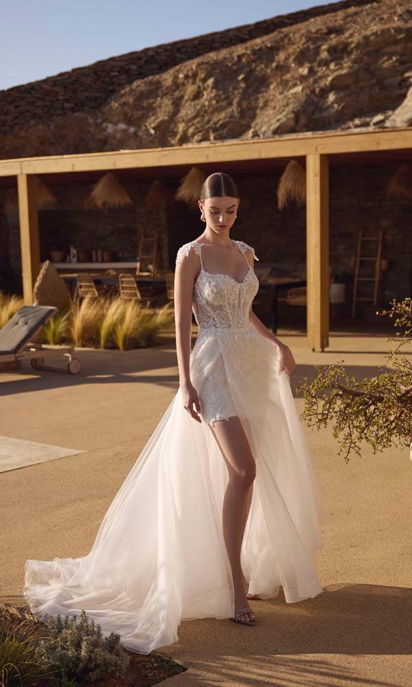 Romantische bruidsjurk met transparante tülloverrok en kort kanten jurkje eronder, gefotografeerd in een warme, mediterrane setting.