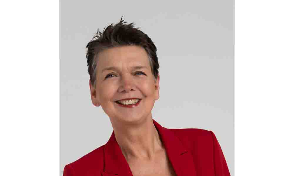 Porträt einer lächelnden Frau mit kurzem dunklem Haar in einem roten Blazer vor hellem Hintergrund.