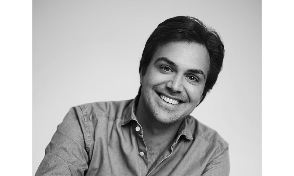 Natürliches Schwarz-weiß-Porträt einer Person mit offenem Lächeln, entspannt in die Kamera blickend.