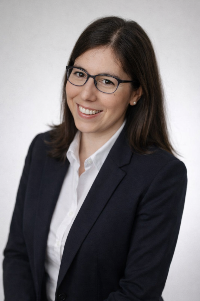 Porträt einer lächelnden Businessfrau mit Brille im dunklen Blazer vor neutralem Hintergrund