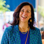 Porträt einer lächelnden Frau mit dunklem Haar in einem blau-grün gemusterten Blazer bei einem Event der Brautmodenbranche