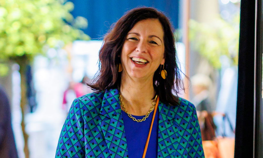 Porträt einer lächelnden Frau mit dunklem Haar in einem blau-grün gemusterten Blazer bei einem Event der Brautmodenbranche