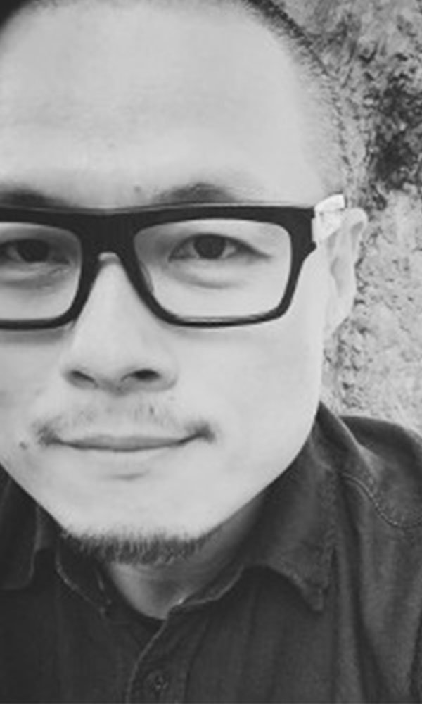 Schwarz-weißes Porträt eines Mannes mit Brille und leichtem Bart, der nah in die Kamera blickt.