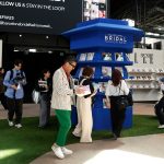 Besucherinnen und Besucher stöbern am Stand der Barcelona Bridal Fashion Week durch Hochzeitsmagazine und tauschen sich in moderner Messeatmosphäre aus.