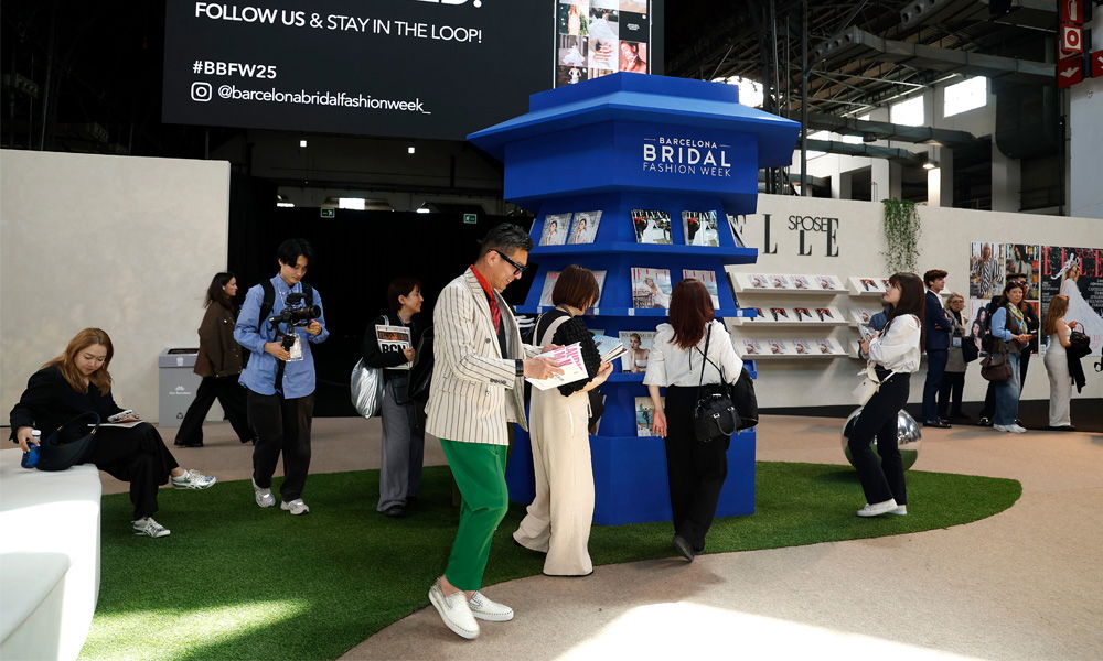 Besucherinnen und Besucher stöbern am Stand der Barcelona Bridal Fashion Week durch Hochzeitsmagazine und tauschen sich in moderner Messeatmosphäre aus.