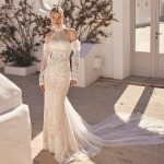 Braut in figurbetontem Spitzenkleid mit langen Ärmeln und Schleppe, fotografiert in mediterraner Kulisse