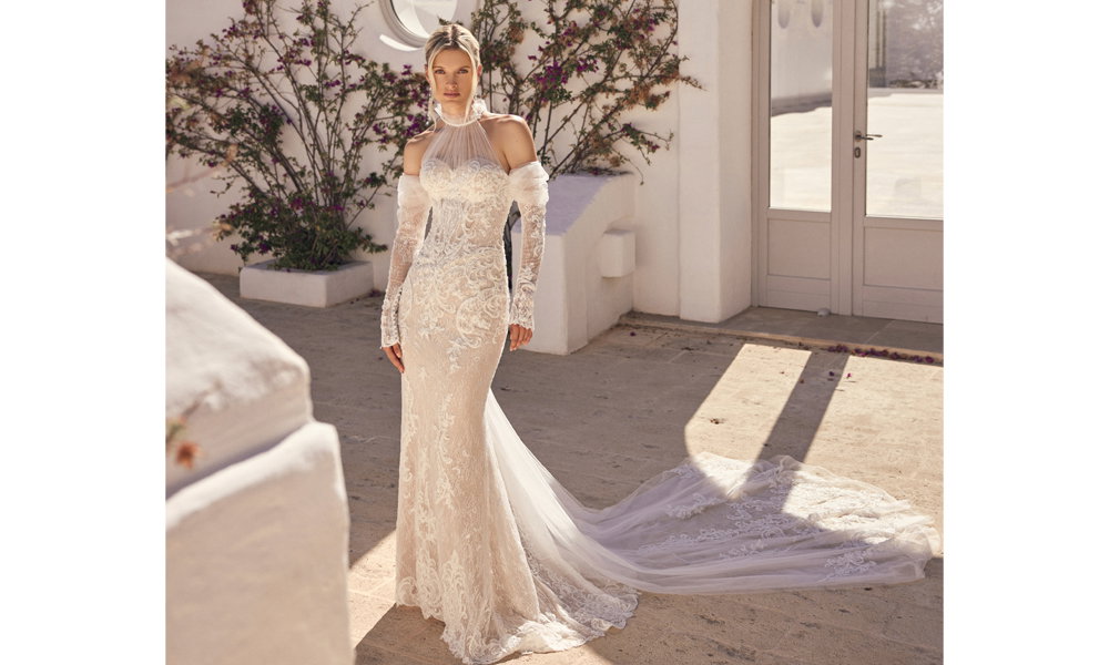 Braut in figurbetontem Spitzenkleid mit langen Ärmeln und Schleppe, fotografiert in mediterraner Kulisse